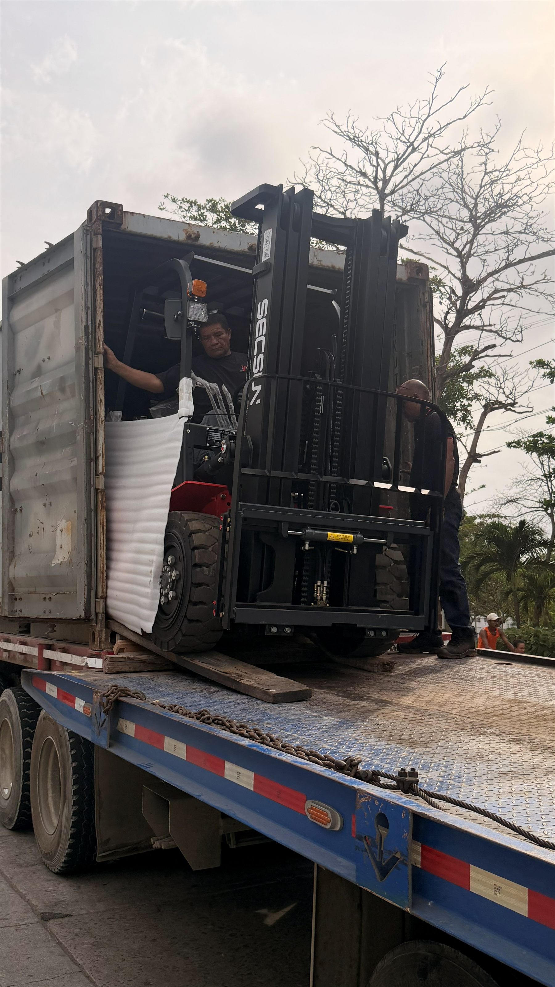 Operarios de YOTA Montacargas descargando un montacargas Secsun FG30 desde el contenedor sobre una cama baja en Barranquilla