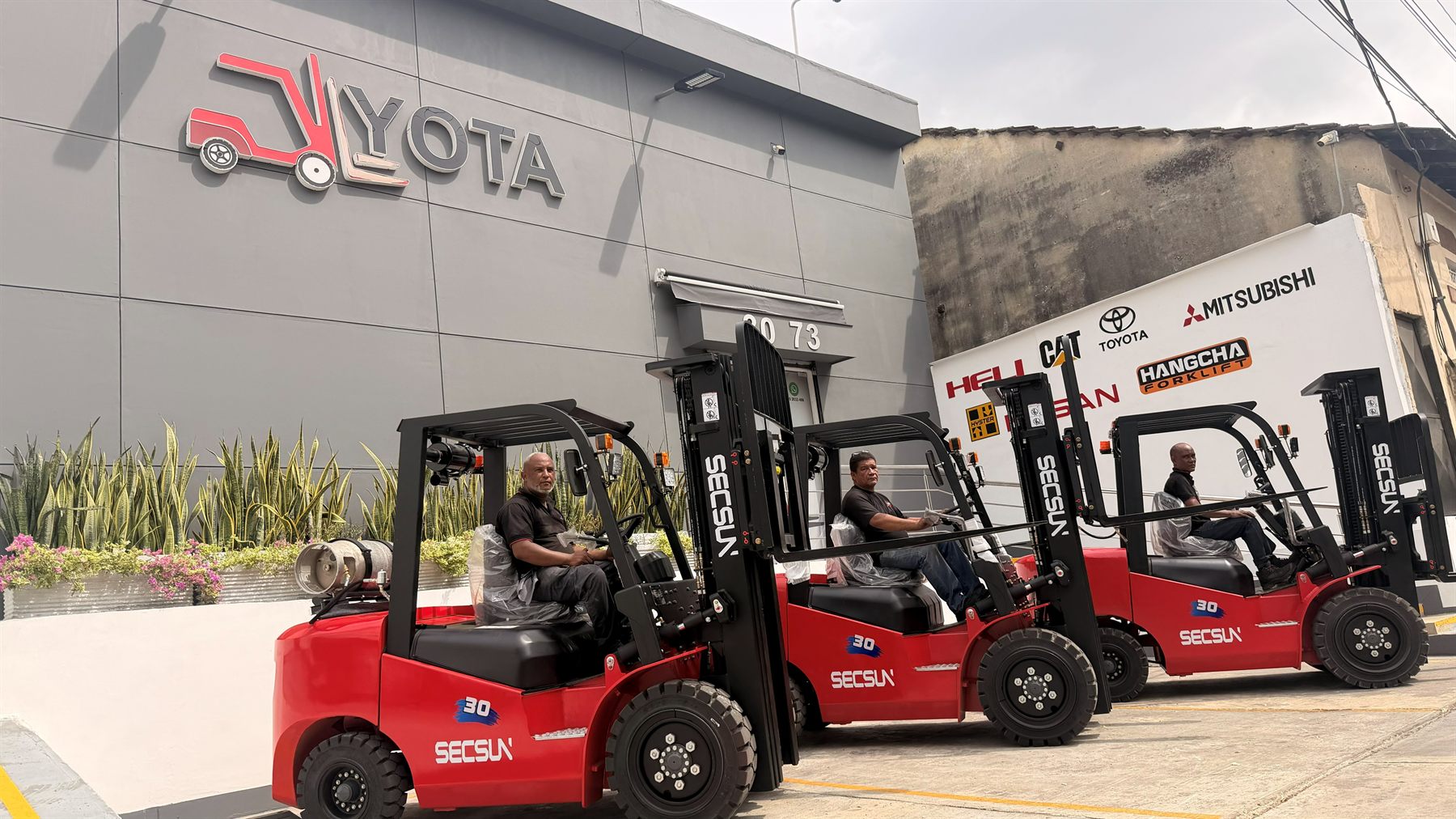 Montacargas Secsun FG30 nuevos frente a la fachada de YOTA Montacargas, con el logo de la empresa y el muro de marcas atendidas