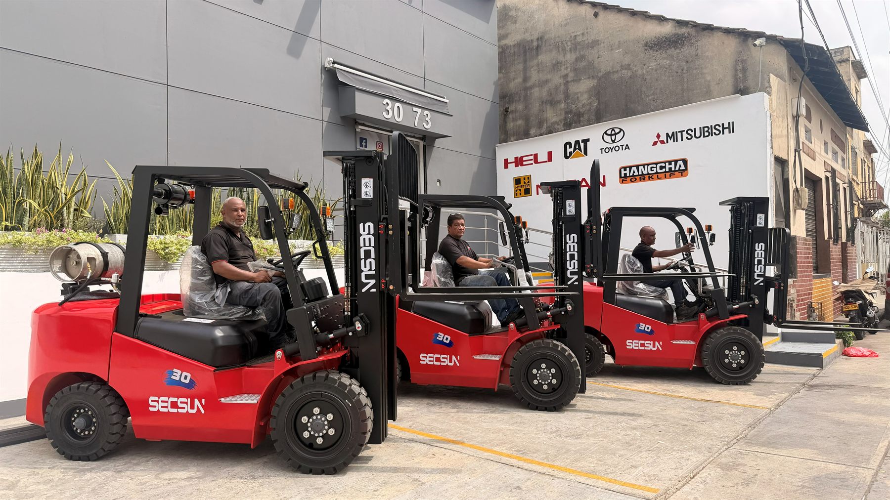 Tres montacargas Secsun FG30 rojos con operadores de YOTA Montacargas sentados en cada uno, frente a la bodega de Barranquilla